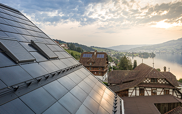 Un toit recouvert de cellules solaires avec à l’arrière-plan les maisons d’un village, des montagnes et un lac