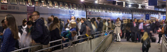 L’immagine mostra uno stuolo di passeggeri assiepati su un marciapiede della stazione di Berna e un treno Intercity delle FFS che entra in stazione.